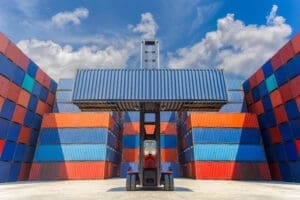 Forklift truck lifting 40 ft new cargo container in shipping yard for transportation import, export and blue sky background.