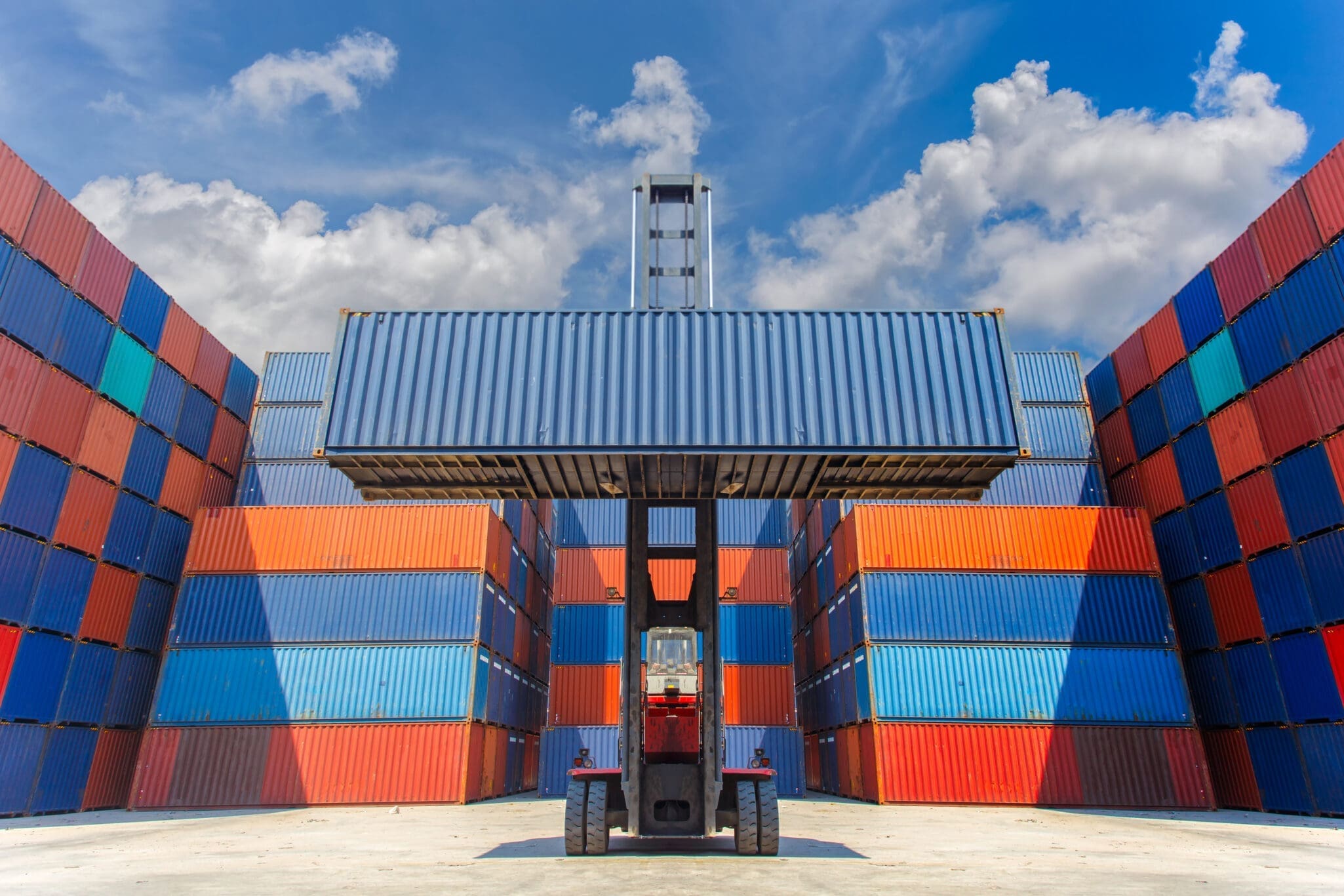 Forklift truck lifting 40 ft new cargo container in shipping yard for transportation import, export and blue sky background.